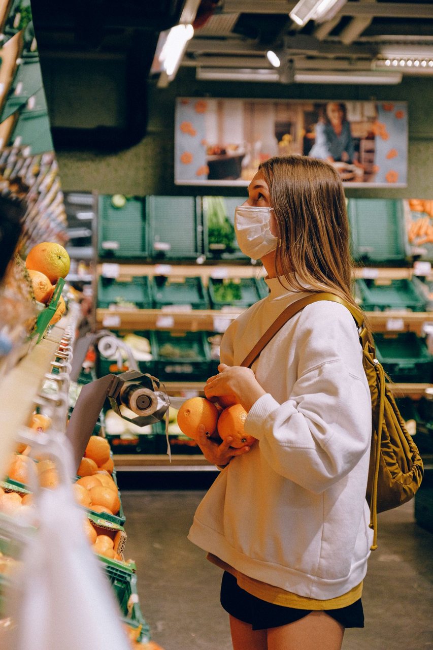 Free Woman in a mask selects fresh oranges in a supermarket, emphasizing hygiene and protection. Stock Photo