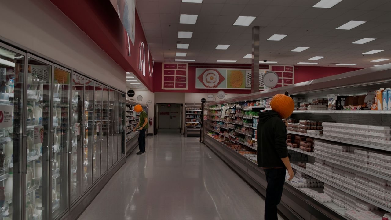 Free Two people wearing pumpkin masks browsing in a supermarket aisle filled with groceries. Stock Photo