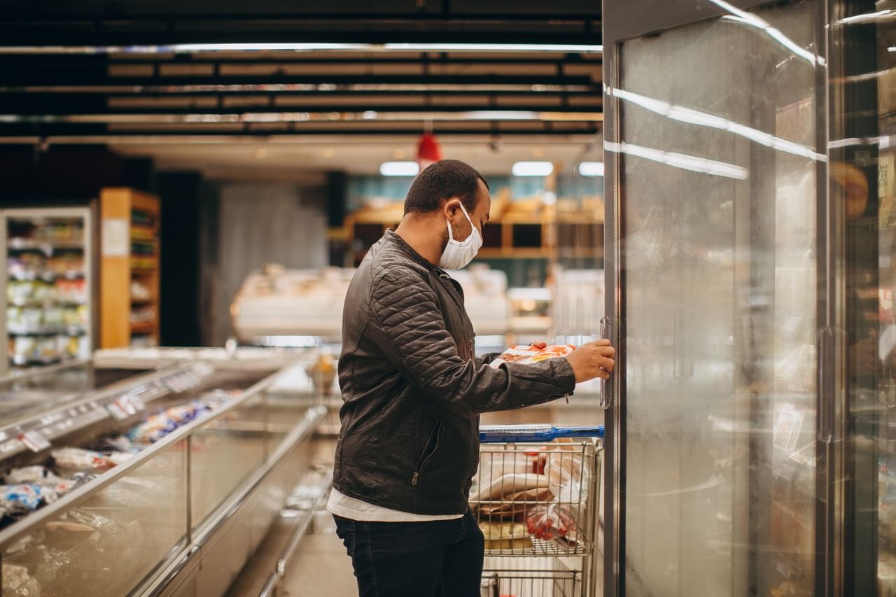 Free A man wearing a mask shops in a supermarket, selecting items from a refrigerated section. Stock Photo